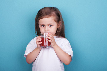 Cute little girl drinking juice from glass on blue background