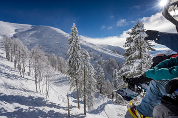 Snowboarders sitting on ropeway, point to the beautiful landscape and ski slopes in the winter resort of Krasnaya Polyana