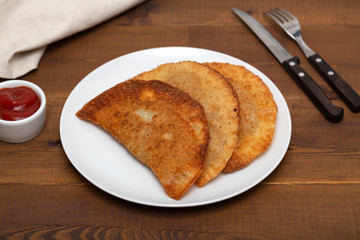 Chebureks - fried pie with meat and onions. White plate with fried chebureks on a wooden table.