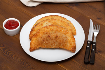 Chebureks - fried pie with meat and onions. White plate with fried chebureks on a wooden table.