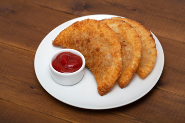 Chebureks - fried pie with meat and onions. White plate with fried chebureks on a wooden table.