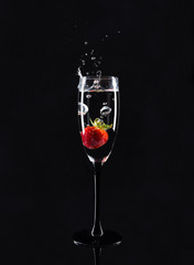 A glass of champagne with a strawberry inside on a black background