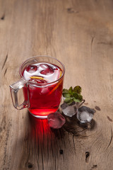 Hibiscus cold tea with ice and mint on vintage wooden background.