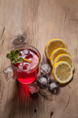 Hibiscus cold tea with ice, lemon and mint on vintage wooden background.