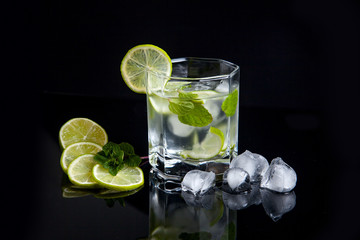 Summer cocktail mojito in glass, sliced lime and ice cubes on black background..