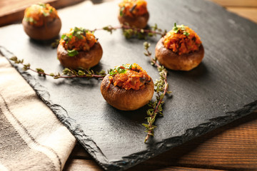 Slate plate with tasty stuffed mushrooms on table