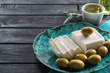 Plate with tasty feta cheese and olives on wooden table