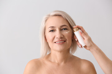 Female hand applying serum onto mature woman's face against light background