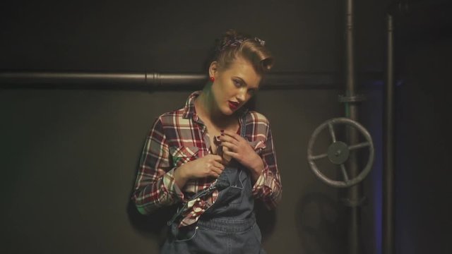 Smiling blonde pin up girl is putting a wrench in her checkered shirt, slow motion