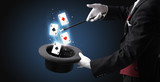 Magician with white gloves conjuring playing cards from a cylinder with magic wand
