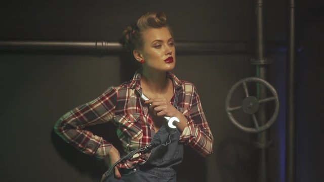 Young pin up girl with s hairstyle is touching her shoulder with a wrench, slow motion