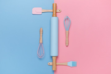 Top view of a stylish rolling pin, whisk, spatula, baking brush on pastel pink and blue background