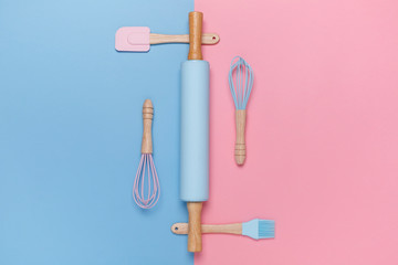 Top view of a stylish rolling pin, whisk, spatula, baking brush on pastel pink and blue background