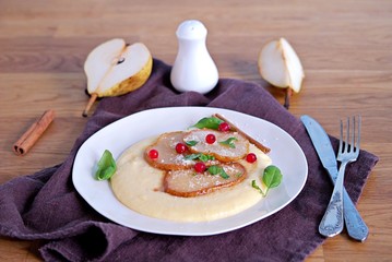 Polenta with cheese, caramelized pear and red currants on a white plate. Italian food. Selective...