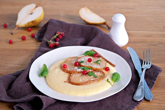 Polenta with cheese, caramelized pear and red currants on a white plate. Italian food. Selective focus.