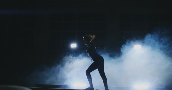 Side view of a female gymnast doing split handstand on balance beam against black background.