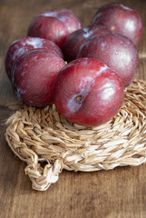 Top view of plums on esparto base and wooden background