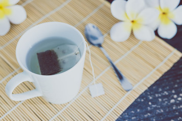 cup of dark tea on bamboo placemat with spoon and flowers all around