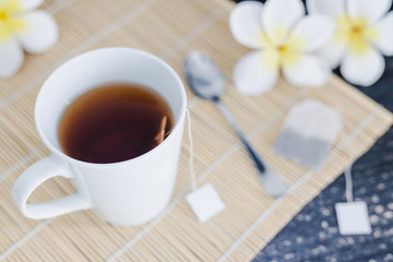 cup of dark tea on bamboo placemat with spoon and flowers all around