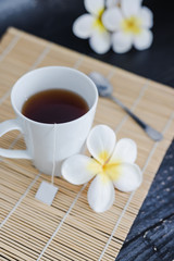 Fototapeta na wymiar cup of dark tea on bamboo placemat with spoon and flowers all around