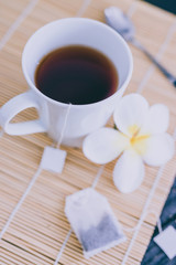 cup of dark tea on bamboo placemat with spoon and flowers all around