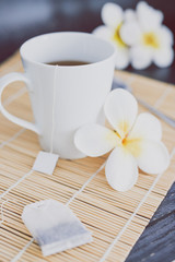 cup of dark tea on bamboo placemat with spoon and flowers all around
