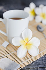 cup of dark tea on bamboo placemat with spoon and flowers all around