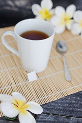 cup of dark tea on bamboo placemat with spoon and flowers all around
