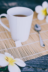 cup of dark tea on bamboo placemat with spoon and flowers all around