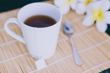 cup of dark tea on bamboo placemat with spoon and flowers all around