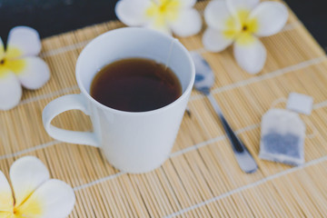 cup of dark tea on bamboo placemat with spoon and flowers all around