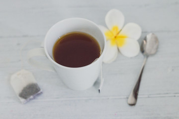 cup of dark tea on wooden table with spoon and flowers all around