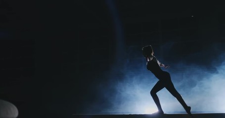 Women's Artistic Gymnastics. In slow motion in the smoke, the girl performs complex elements of the Olympic program on a balance beam.
