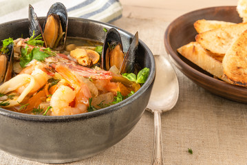 Homemade cioppino in a bowl and toast - Italian-American seafood soup - fish, mussels, shrimps and squids.