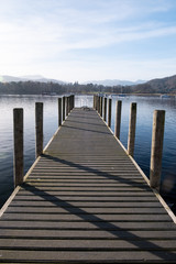 Fototapeta premium The pier at Ambleside Waterhead on a clear day looking over the Great Langdale skyline, Lake District, UK