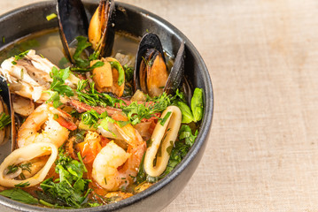 Homemade cioppino in a bowl and toast, top view, copy space for a recipe - Italian-American seafood soup - fish, mussels, shrimp and squid.