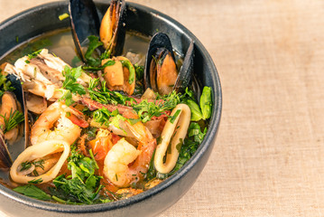 Homemade cioppino in a bowl and toast, top view, copy space for a recipe - Italian-American seafood soup - fish, mussels, shrimp and squid.