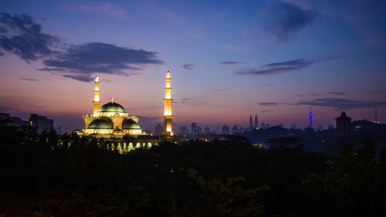 Fototapeta premium The Federal Territory Mosque during sunrise with Kuala Lumpur city skyline on the background.