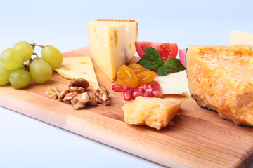 Assortment of cheese with fruits, grapes, nuts and cheese knife on a wooden serving tray.