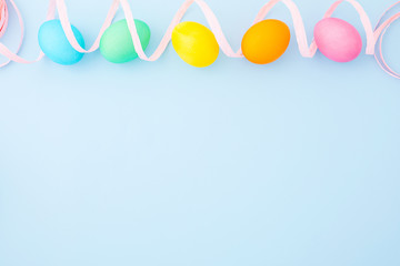 Colorful Easter eggs with pink ribbon on a light blue background. Flat lay. Top view. Copy space