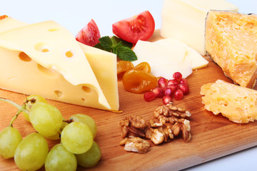 Assortment of cheese with fruits, grapes, nuts and cheese knife on a wooden serving tray.