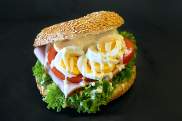 Sandwich with egg, lettuce, tomato and ham. On a dark background
