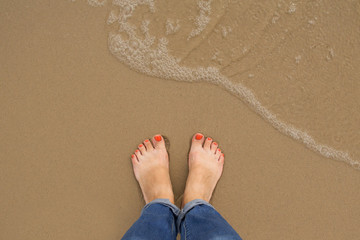 Orange nail pedicure Feet of female stand on the summer sand beach, top view, Woman solo travel...