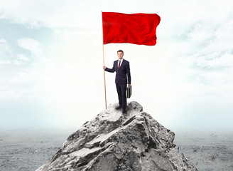 Obraz premium Handsome businessman on the top of the mountain with red flag 