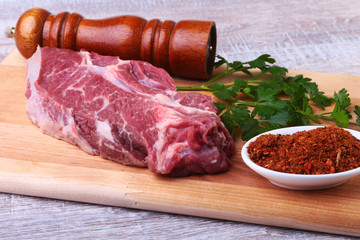 Raw beef steak with spices Leaves of coriander on wooden cutting board. Ready for cooking.