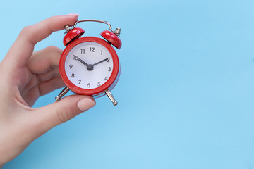 The alarm clock in female hand on a color background with free space for text