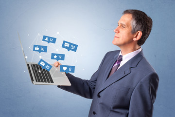 Man holding laptop with different types of social media symbols and icons
