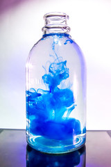 Art shot of a transparent vase with a plant with clear water and color ink paint in the studio with lighting. The concept of experiments in the scientific laboratory.