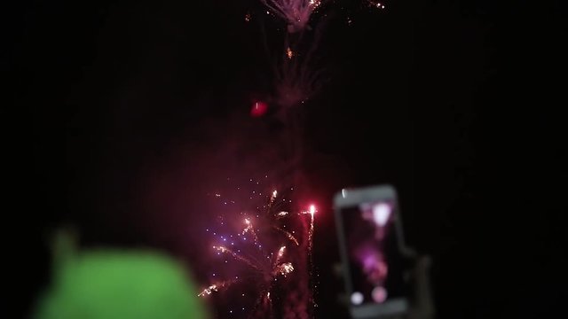 Amazing firework show. People shoots salute on a mobile phone. Bright splashes of flowers of salute against night sky.