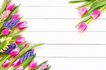 Spring flowers border on white wooden background. Top view, copy space. Greeting card.